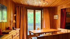A wooden cabin with a dining table and chairs, a kitchen area with cabinets, and a large window with curtains. - Chalet-style apt 4/5 pers, center of resort, 50m from slopes (Pra-Loup)
