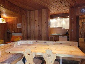 A wooden interior with a dining table and chairs, a kitchen area with cabinets, and a clock on the wall. - Chalet-style apt 4/5 pers, center of resort, 50m from slopes (Pra-Loup)
