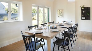 Un comedor con una mesa de madera dispuesta para seis personas, rodeada de sillas negras, con ventanas amplias y vistas al exterior.
