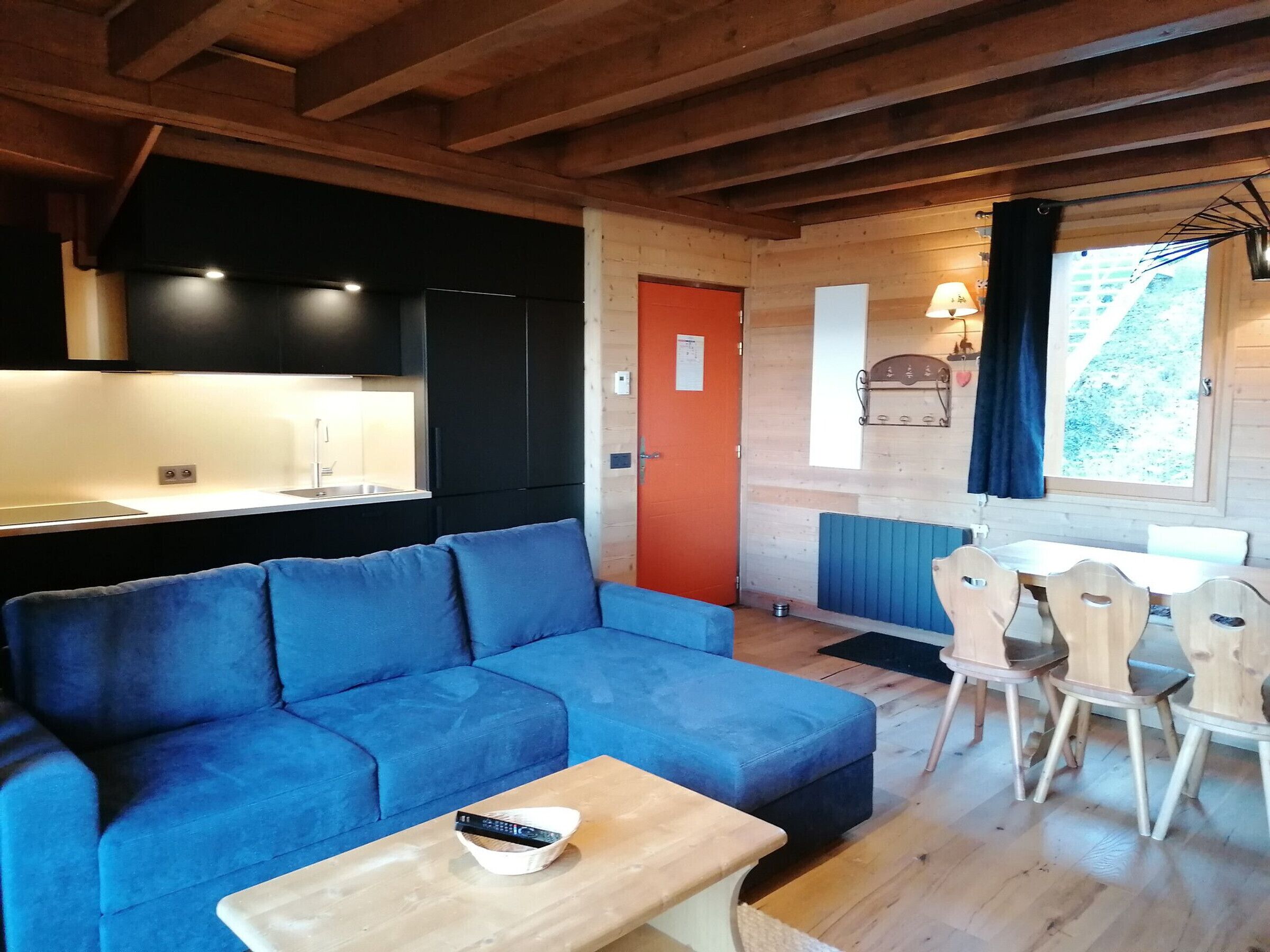 Interior acolhedor de uma cabana, com um sofá azul, mesa de jantar de madeira e uma cozinha compacta.