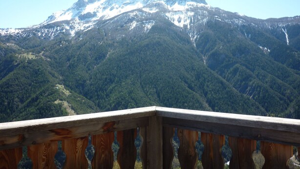 A mountain landscape with a wooden balcony railing.