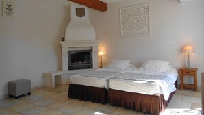 Een slaapkamer met een open haard, twee nachtkastjes met lampen, een bed met dekbed en bedrok, en een decoratieve muur met patroon.