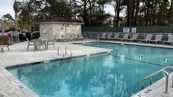 A swimming pool with a lifeguard station, lounge chairs, and a small building.