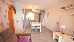 A modern living room with a brown sofa, a dining area with a white table and chairs, and a small white side table with a lamp. - ACARI0406-1ºlínea Playa-Wifi y Garaje Gratis. (Calpe)