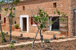A rustic building with a stone facade, wooden shutters, and a paved courtyard with trees and stepping stones. - Can Cortana 005 fantastic finca with private swimming pool, children's area, ping pong and air conditioning (Llubi)