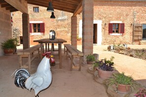 A rustic outdoor patio with a wooden table and benches, surrounded by potted plants and a rooster. - Can Cortana 005 fantastic finca with private swimming pool, children's area, ping pong and air conditioning (Llubi)