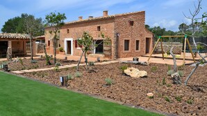 A rustic house with a stone facade, a patio area with a swing set, and a well-maintained garden with mulch and small plants. - Can Cortana 005 fantastic finca with private swimming pool, children's area, ping pong and air conditioning (Llubi)