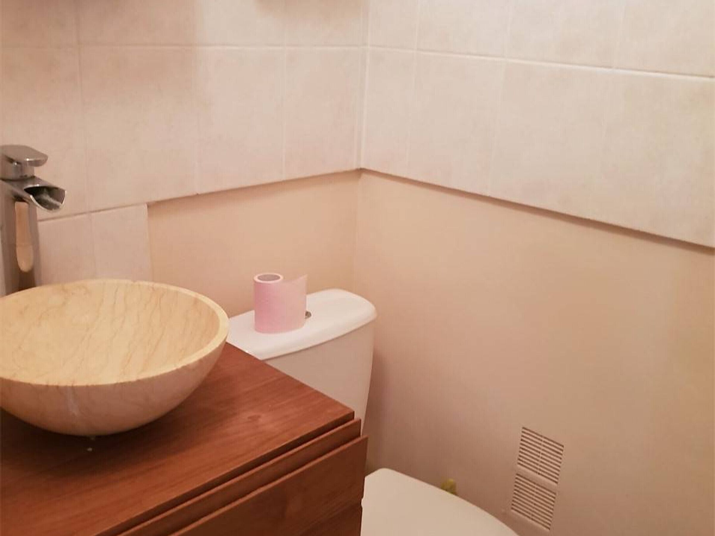 A bathroom with a wooden vanity, a toilet, and a roll of toilet paper.