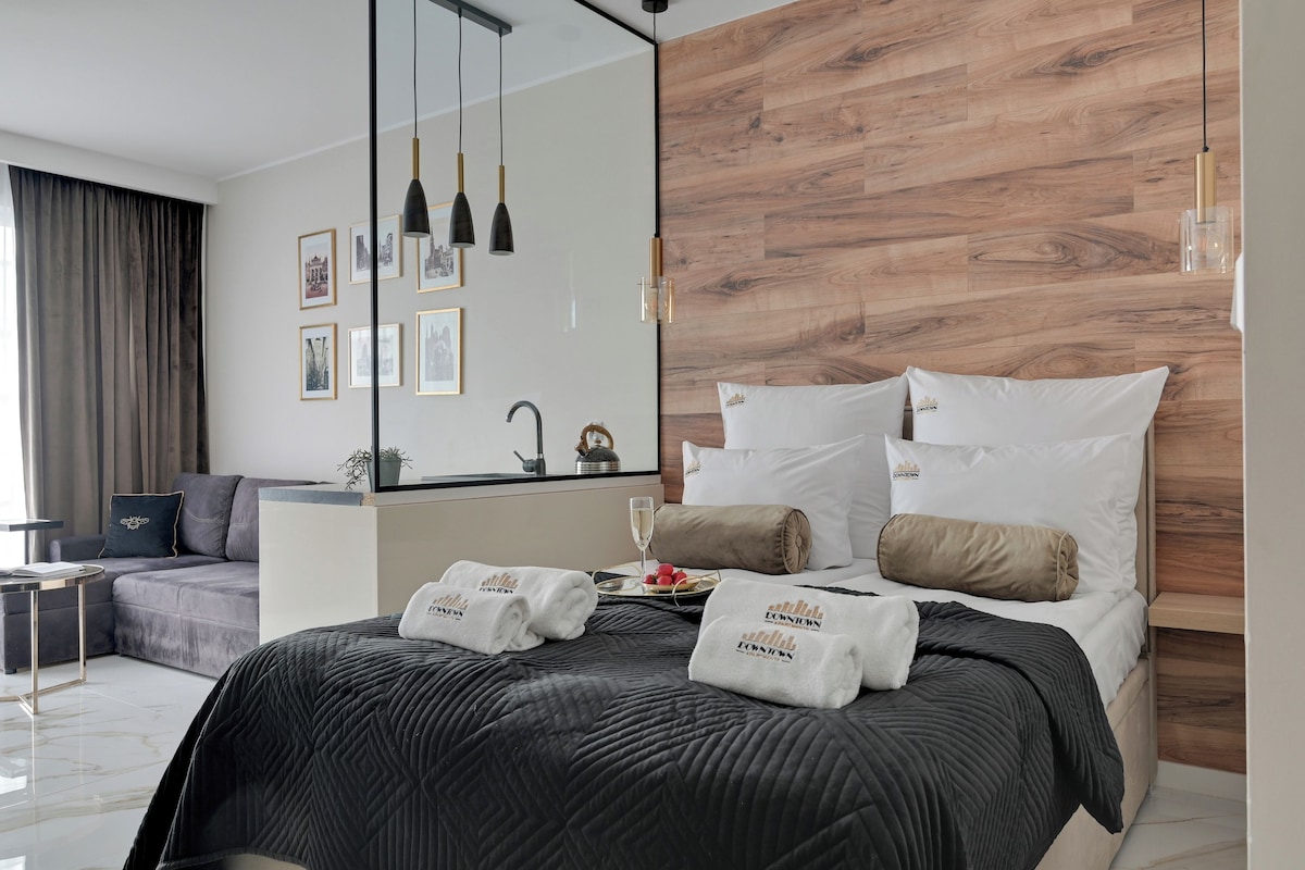 A modern hotel room with a large bed, a sofa, a dining table, and a mirror.