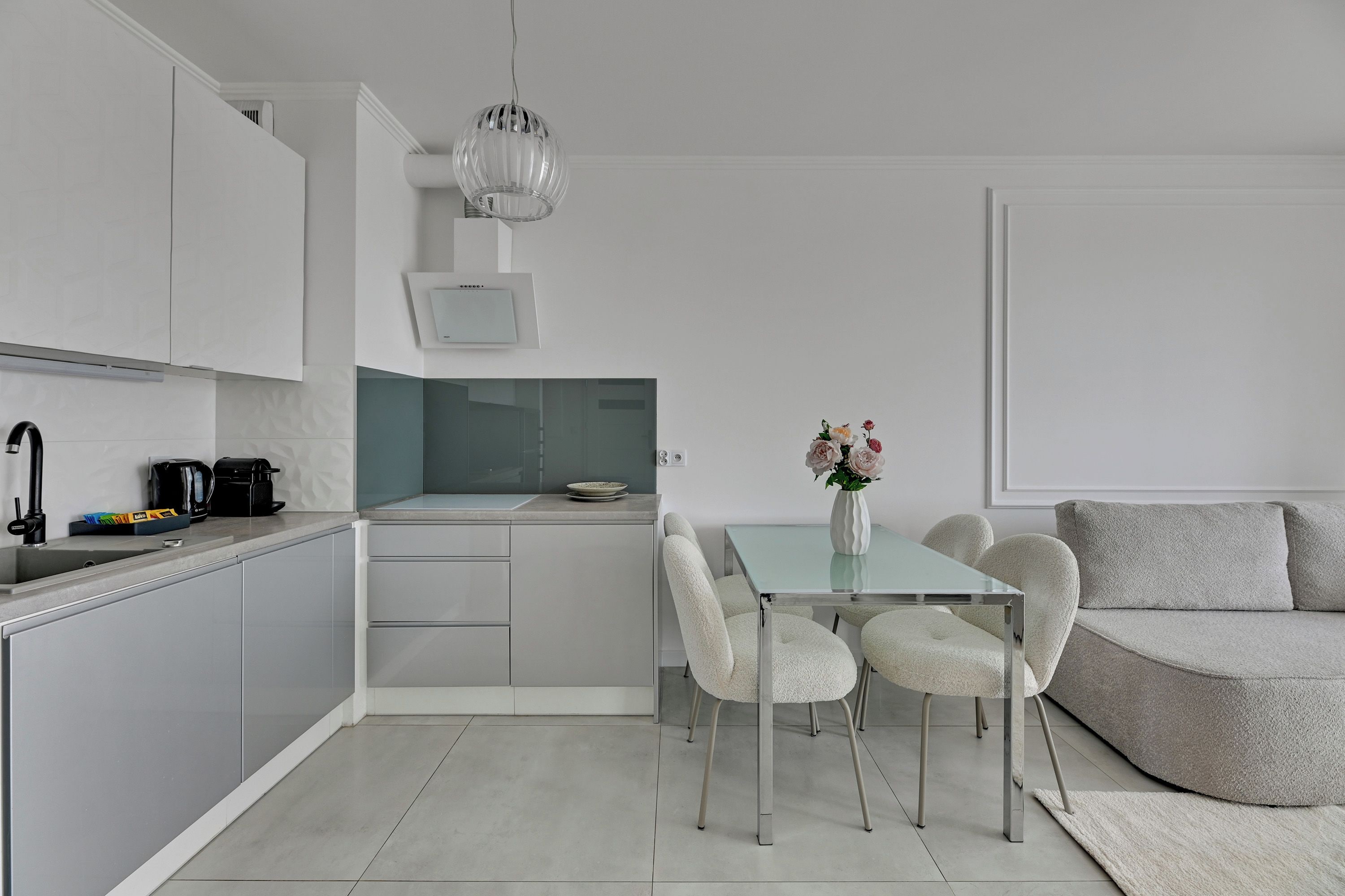 Une cuisine moderne avec des meubles blancs, une table à manger avec des chaises et un petit coin cuisine.