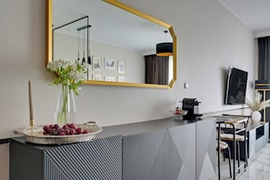 A modern living room with a large mirror, a dining area with striped chairs, and a coffee machine on the counter. - Bastion Wałowa City Center by Downtown Apartments (Gdansk)