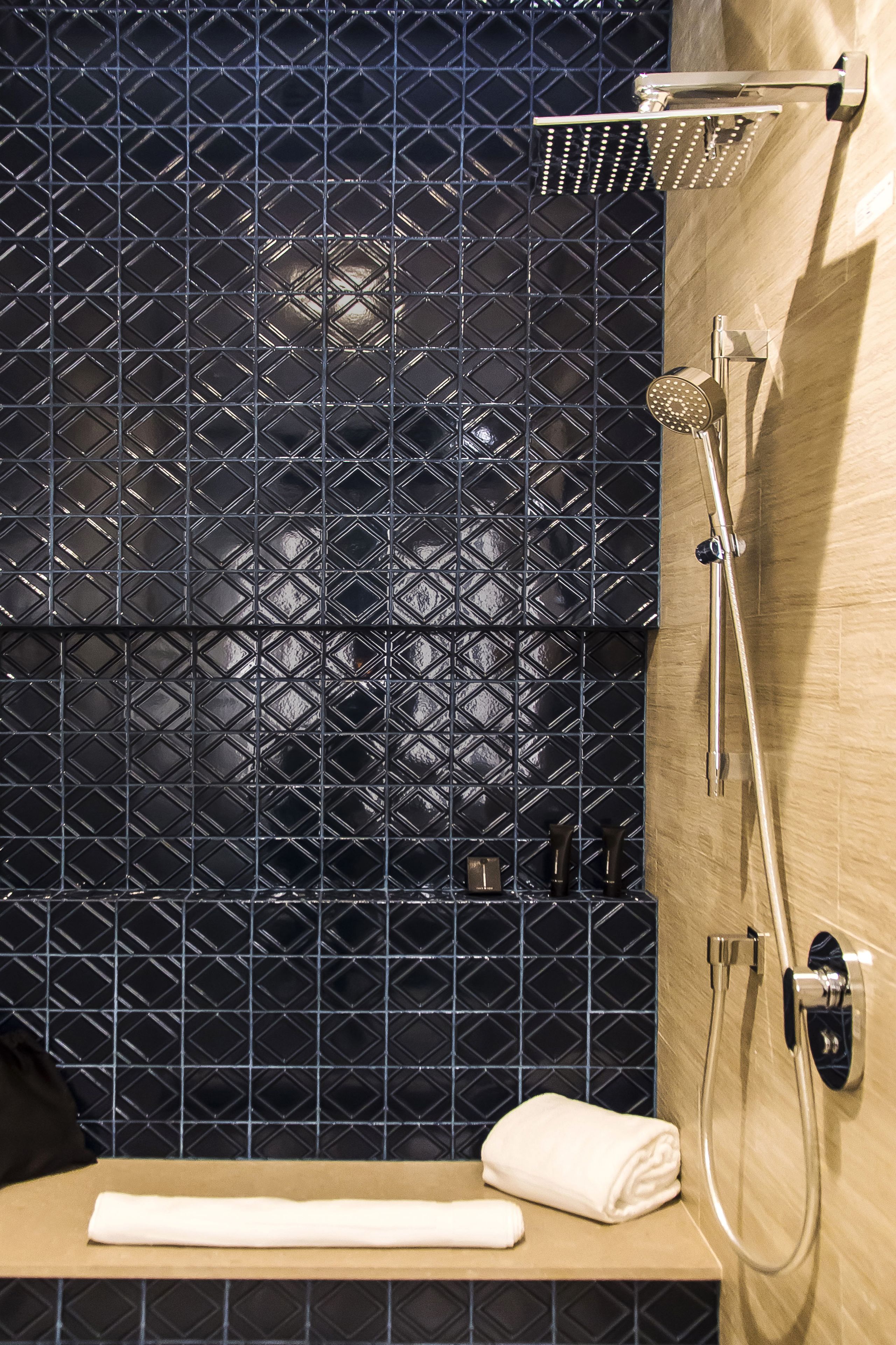 A bathroom with a black diamond-patterned tile wall, a wooden countertop, a white towel, and a shower with a handheld showerhead.