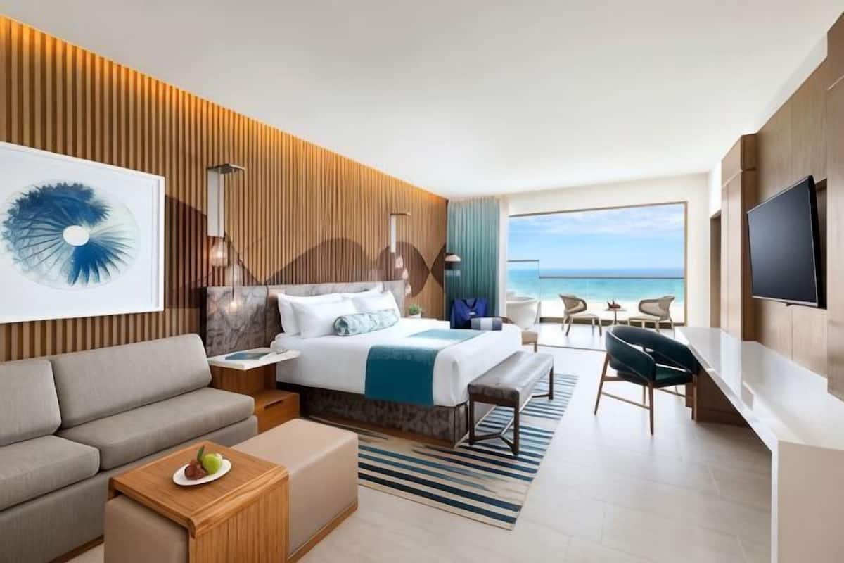 A modern hotel room with a bed, a sofa, a desk, and a TV.