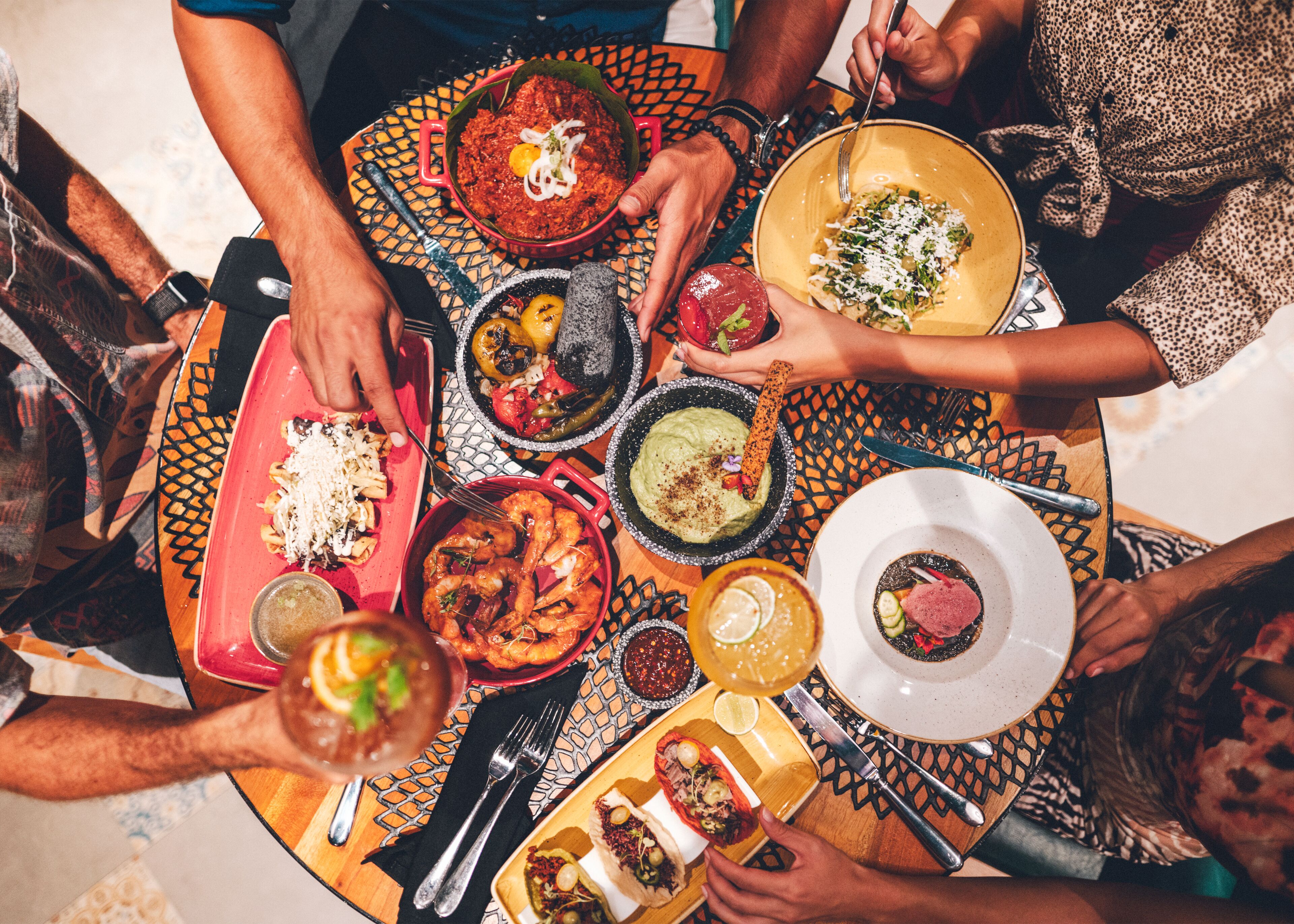 A group of people around a table with various dishes, including seafood, pasta, and a bowl of guacamole.