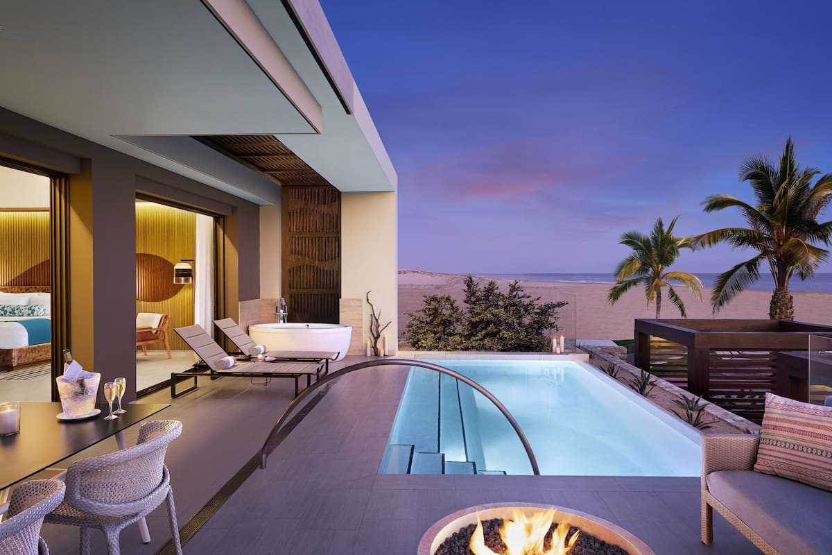 A modern hotel suite with a private pool, lounge chairs, and a fire pit.