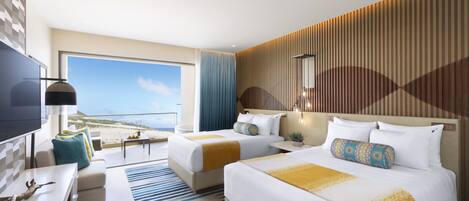 Habitación de hotel con dos camas, televisión, escritorio y vista a la playa.
