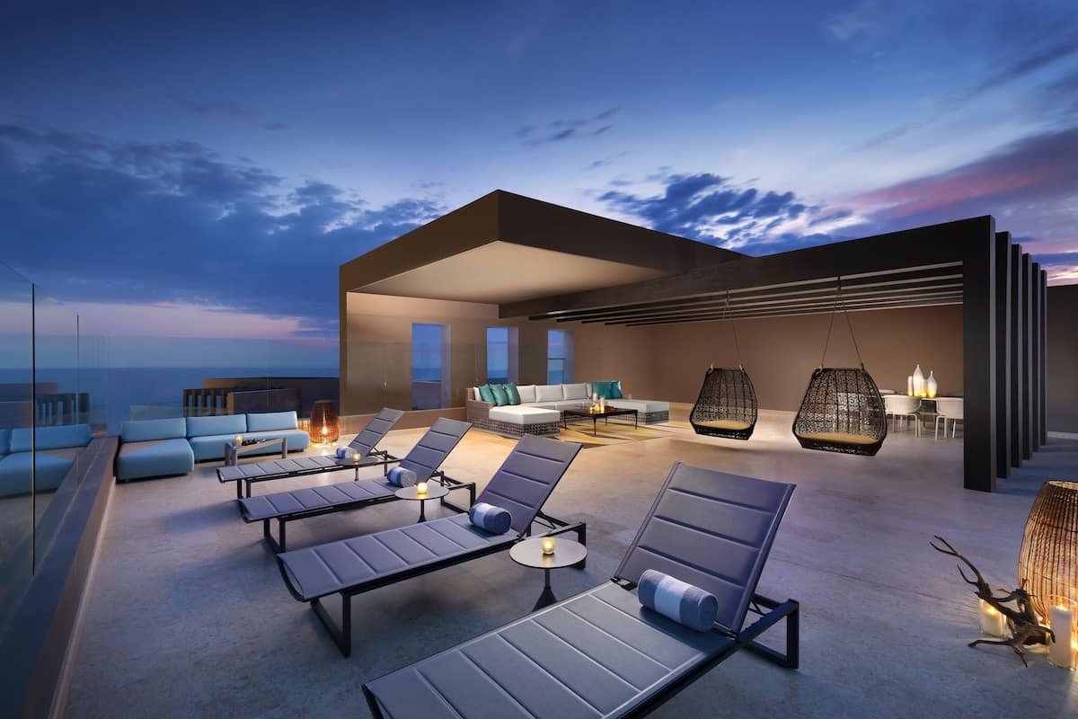 A rooftop lounge with sun loungers, a sofa, and a dining area.