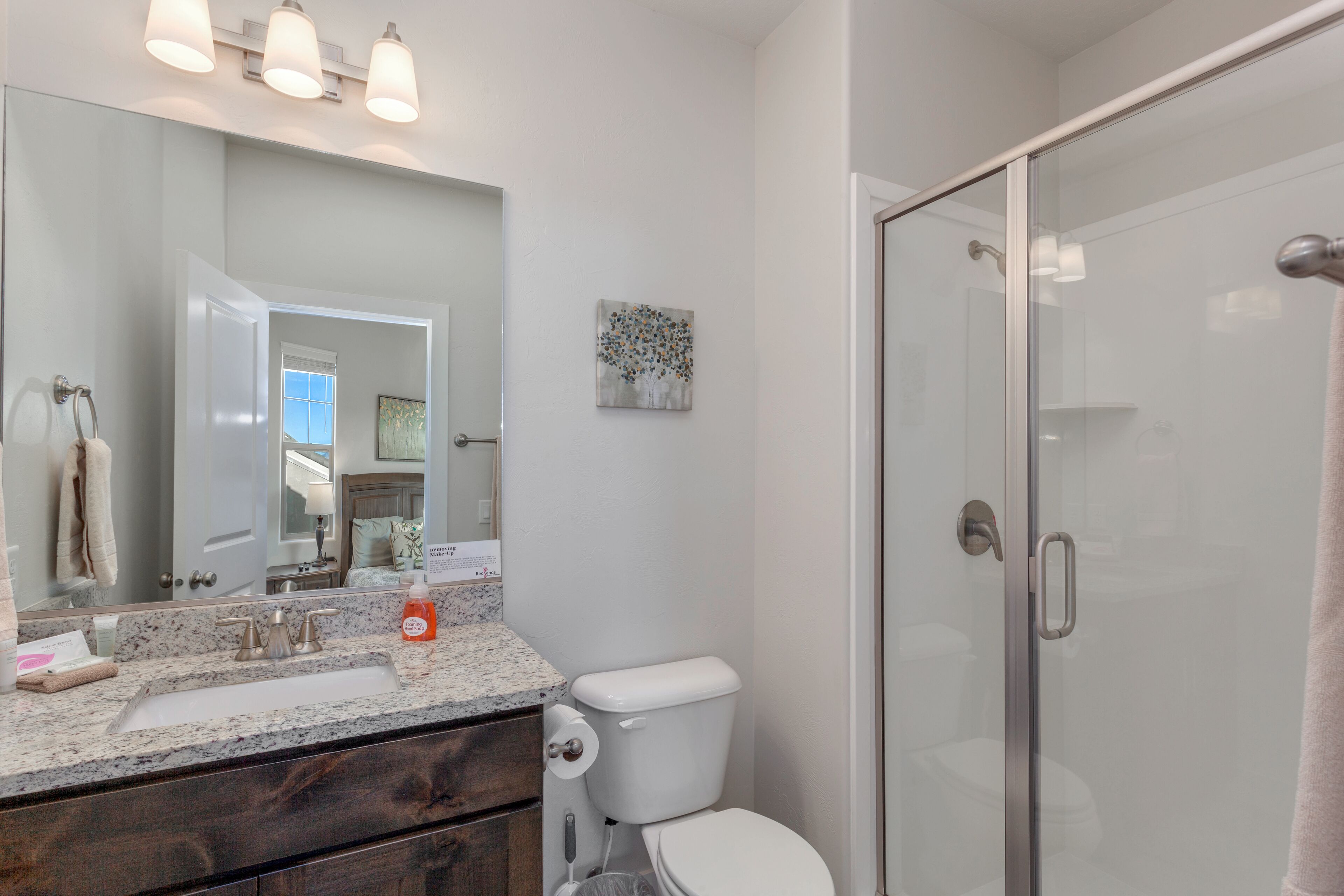 Une salle de bain dotée d’une douche à parois de verre, de toilettes, d’un lavabo avec un plan de travail en marbre et d’un grand miroir.