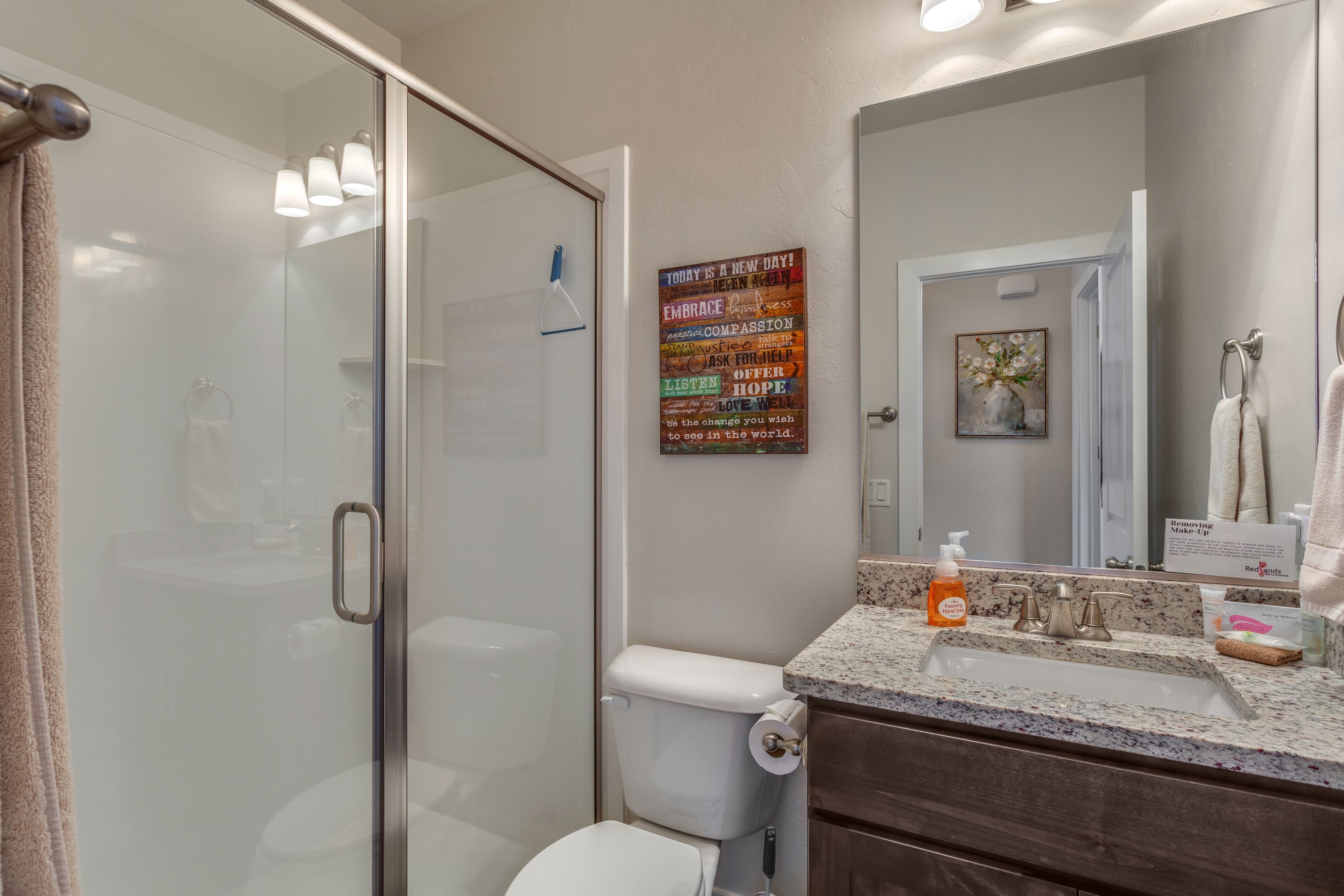A bathroom with a glass shower enclosure, a toilet, a sink with a marble countertop, and a large mirror.