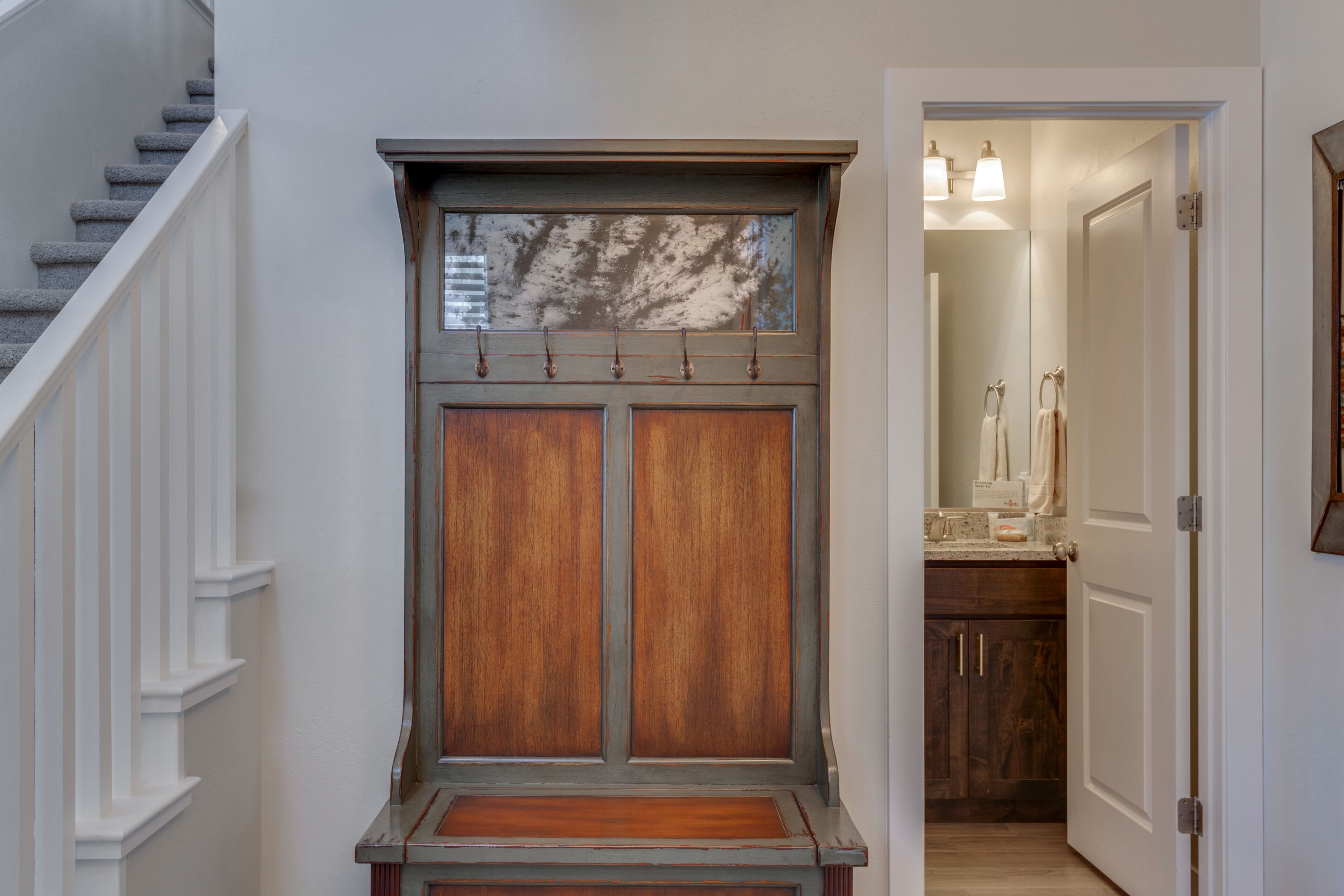 Un pasillo con una puerta de madera, una escalera y una zona de cocina visible a través de una puerta abierta.