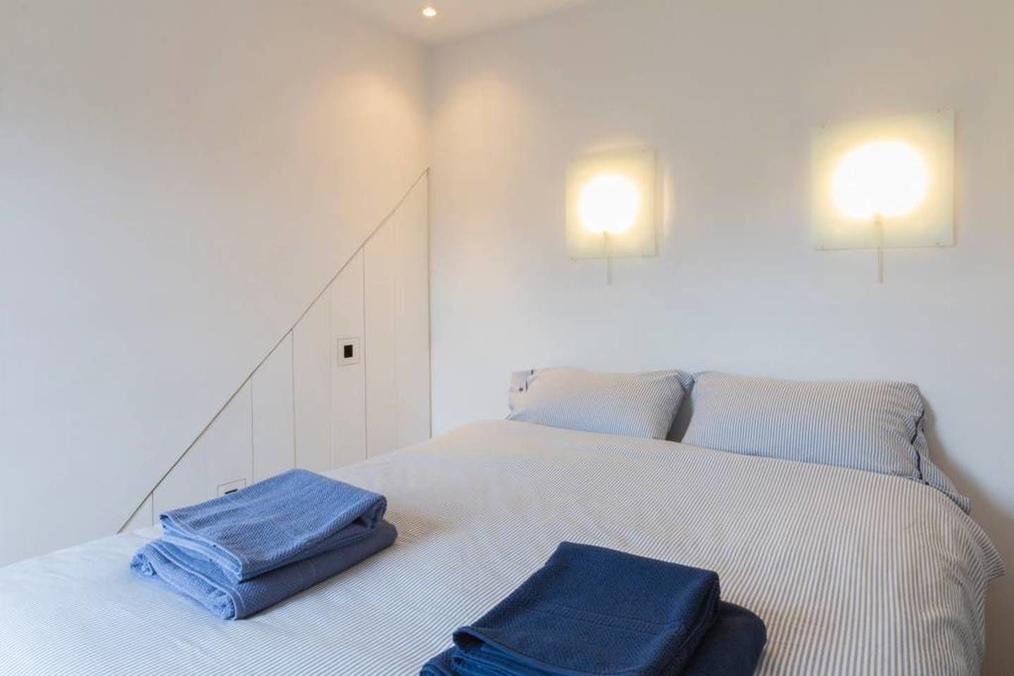 Ein Hotelzimmer mit einem Bett, zwei Wandleuchten und einem gefalteten Handtuch auf dem Bett.