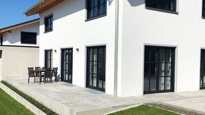A modern two-story house with a patio, large windows, and a well-maintained lawn.
