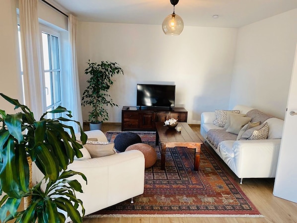 A living room with a sofa, a coffee table, a TV, and a large plant.
