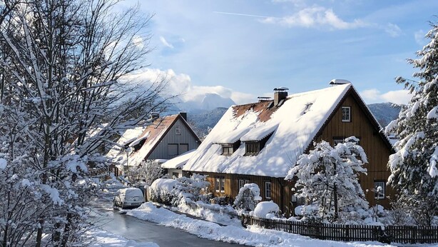 A snow-covered village with traditional wooden houses, a clear road, and a mountain backdrop.