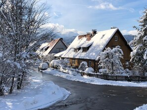 Un villaggio innevato con case in legno tradizionali, una strada sgombra e montagne sullo sfondo.