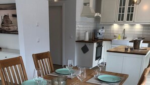 A dining area with a wooden table set for four, equipped with turquoise plates, glasses, and cutlery. The chairs have grey cushioned seats.