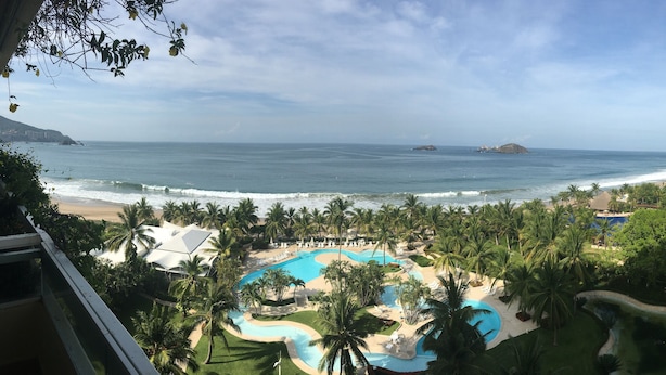 Un complexe hôtelier doté d’une piscine, de palmiers et offrant une vue sur l’océan.