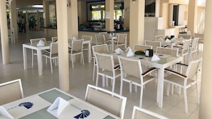 Un restaurant avec des tables et des chaises blanches, un coin bar et un ventilateur de plafond.