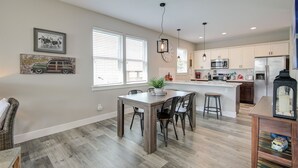 Una cocina moderna con una isla central, armarios blancos y un comedor con mesa y sillas de madera.