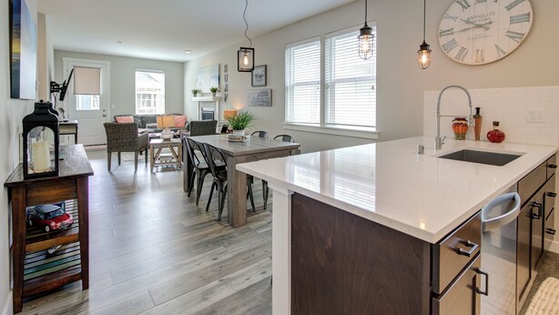 Una cocina moderna con una isla grande, mesa de comedor de madera y sillas. Hay un reloj en la pared y una lámpara colgante.