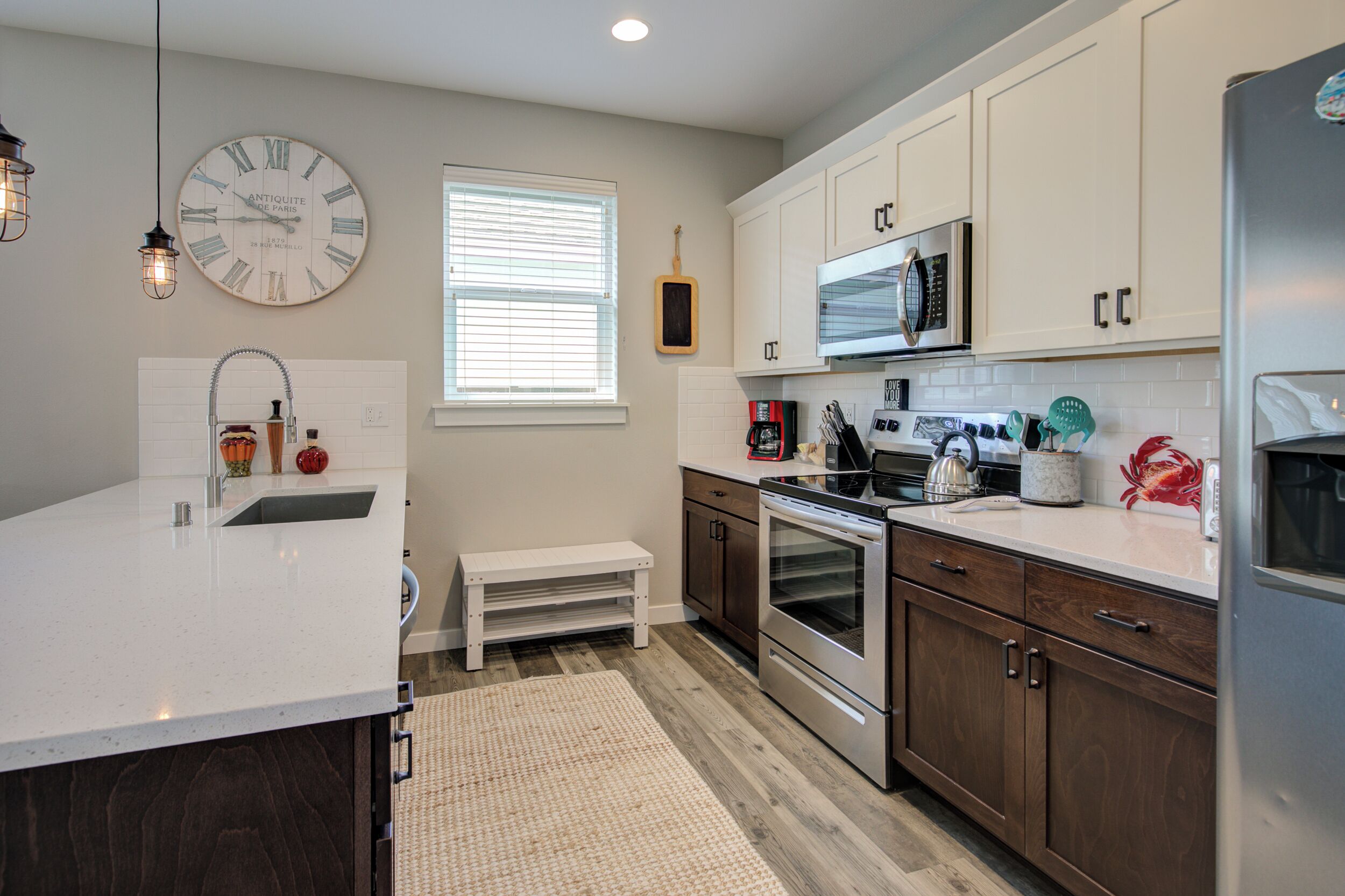 A modern kitchen with white cabinetry, stainless steel appliances, a large wall clock, and a small wooden bench.