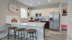Una cocina moderna con armarios blancos, electrodomésticos de acero inoxidable, una isla grande con taburetes y un reloj de pared.