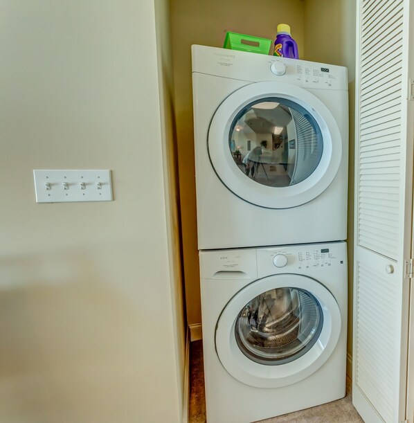 A front-loading washer and dryer stacked in a laundry room with a light switch on the wall.