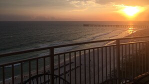 Ein Sonnenuntergangsblick von einem Balkon mit Blick auf einen Strand und einen sich ins Meer erstreckenden Steg.