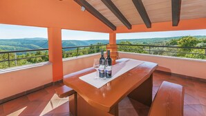 Une table en bois, sur laquelle sont posées deux bouteilles et deux verres, le tout sur un tapis blanc. De là, on peut admirer un paysage magnifique.
