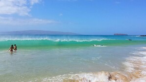 A beach with clear turquoise water, a sandy shore, and a distant mountain. -  'Island Casual' Oceanfront  'Elegantly Comfortable'  (Wailuku)