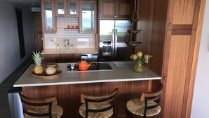 A modern kitchen with wooden cabinets, a stainless steel refrigerator, and a central island with bar stools. -  'Island Casual' Oceanfront  'Elegantly Comfortable'  (Wailuku)