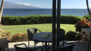 A patio with a table and chairs, overlooking a view of the ocean and a well-maintained lawn. -  'Island Casual' Oceanfront  'Elegantly Comfortable'  (Wailuku)