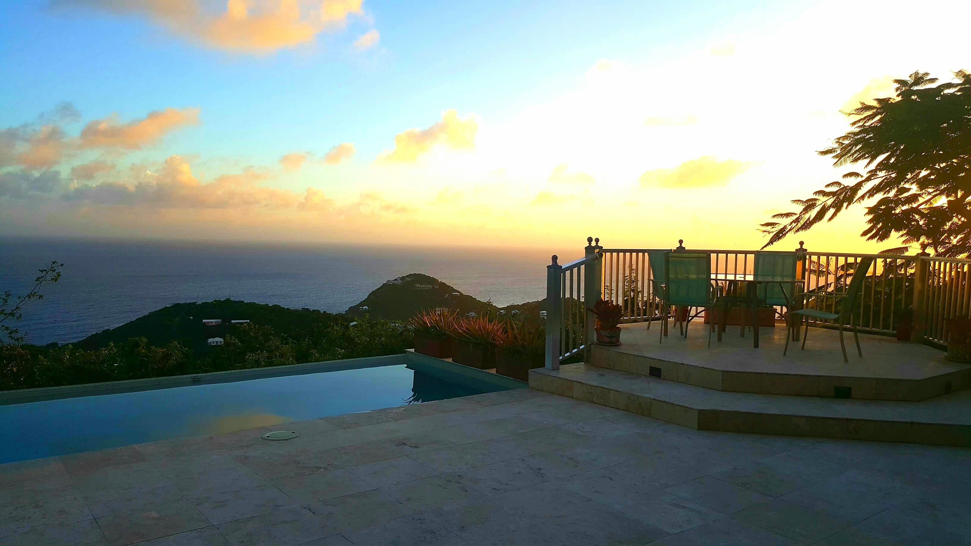 A poolside area with a view of the ocean and a sunset.