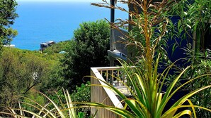Une maison située sur la côte, avec vue sur l’océan, entourée d’une végétation luxuriante et agrémentée de plantes en pot.