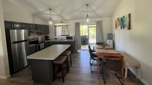 Et moderne køkken med en central ø, rustfrie hårde hvidevarer og et spiseområde med et træbord og stole.