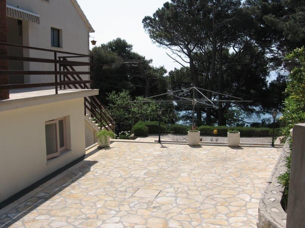 Un patio empedrado con cerca de madera, una pérgola y un gran árbol.
