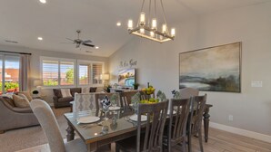 A dining area with a glass table, wooden chairs, and a chandelier. There is a ceiling fan and a painting on the wall. - Paradise Village Resort 86, Private Hot Tub, Game System, Community Amenities, and more (Santa Clara)