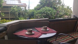 A balcony with two chairs, a table, and two cups on placemats. - One Bedroom, First Floor, Fully Furnished Condo (Kailua-Kona)