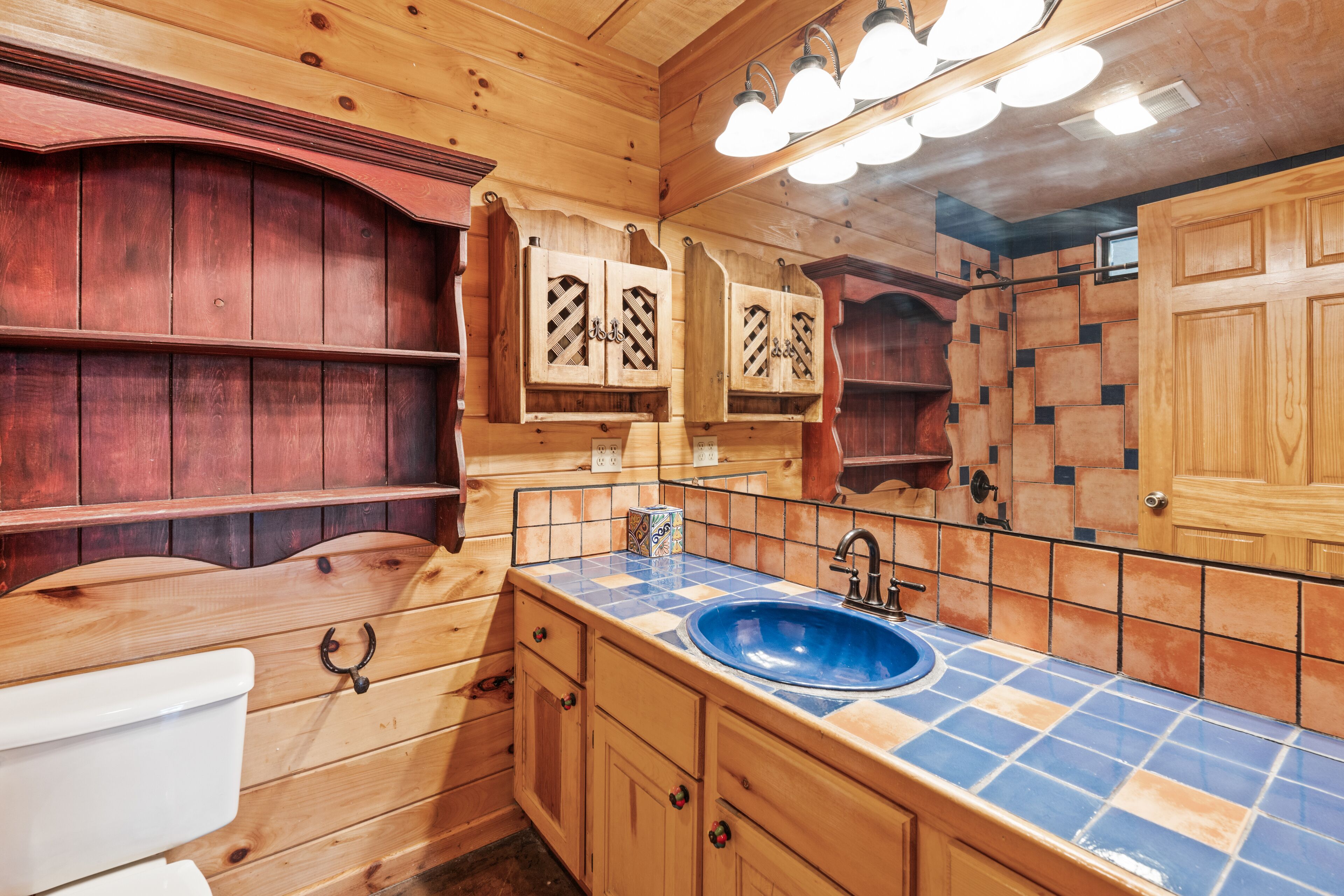A wooden bathroom with a blue and orange tiled sink, wooden cabinets, and a mirror above the sink.