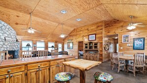 Ein Holzhütten-Interieur mit Kamin aus Stein, Esstisch aus Holz, Barhocker und Deckenventilatoren.